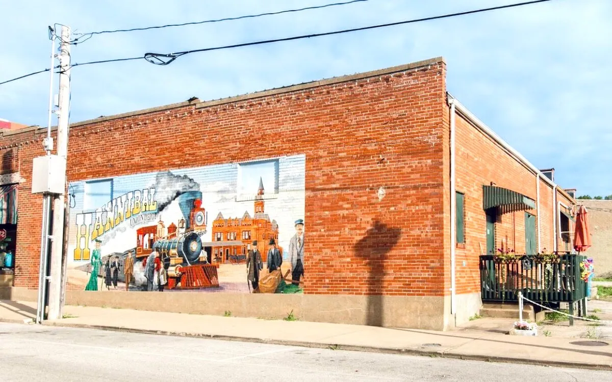 A historic brick wall adorned with a colorful mural, paired with an outdoor seating area and street lamp. The setting is ideal for enjoying local cuisine, snapping photos, or soaking in Hannibal’s unique culture.