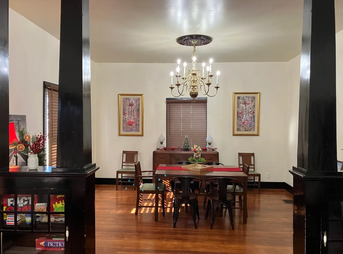 A stylish dining room with a central dining table under a chandelier, artwork on the walls, and decor on the sideboard. The mood is warm and welcoming, suggesting a space ideal for family gatherings and shared meals.