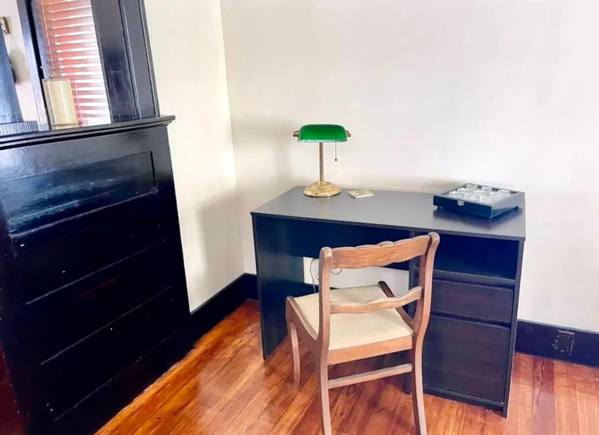 A serene home office nook featuring a sleek black desk, a classic green lamp, and a wooden chair. The setup is minimal, inviting, and purpose-built for productivity, offering an ideal workspace for business travelers or guests needing a quiet corner for creative pursuits.